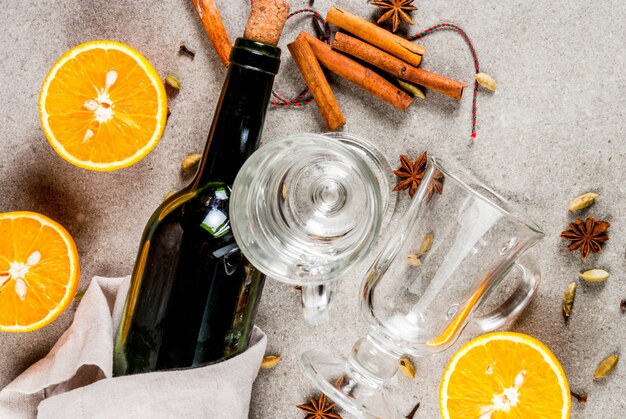 Christmas hot drinks recipes, Set of ingredients for mulled wine: wine bottle, glass cups, spices, orange. Gray stone ,  top view