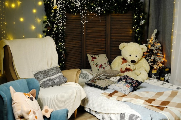 In the Christmas interior of the room there is a large bed with soft toys and pillows next to the bed there is an armchair Children's New Year's photo zone