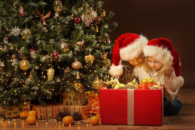 Christmas Kids with Big Red Gift Box full with Present Toys Two Little Girls next to Xmas Tree