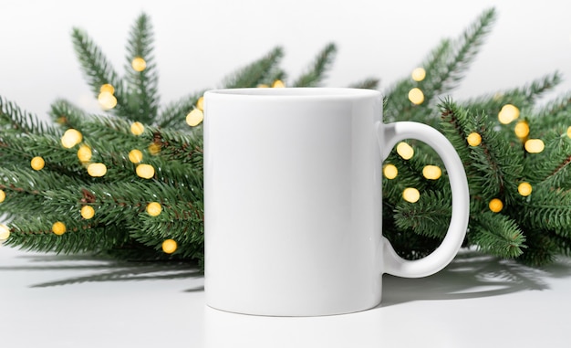 Christmas mockup one white empty tea mug on a white table and branches of a Christmas tree wreath.