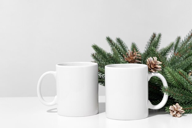 Christmas mockup white empty tea mugs on a white table and branches of a Christmas tree wreath.