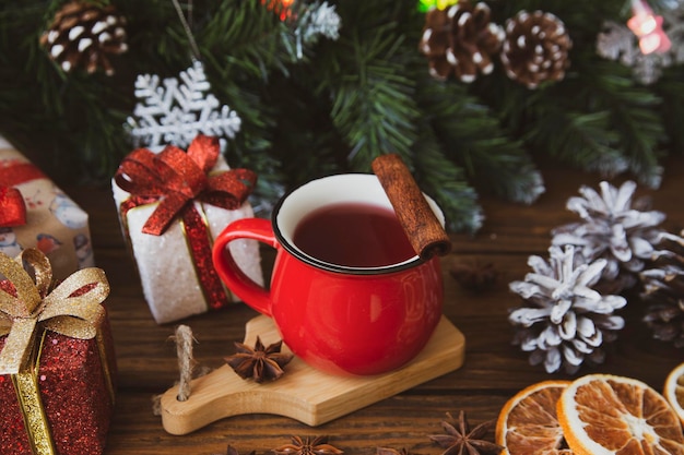 Christmas mood holiday atmosphere Red cup of coffee fir branches with cones Christmas gifts star anise on a wooden table background