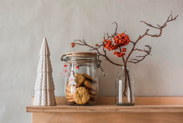 Christmas mood in the interior Ceramic Christmas tree dried flowers in a glass bottle a jar of oatmeal cookies on a wooden shelf