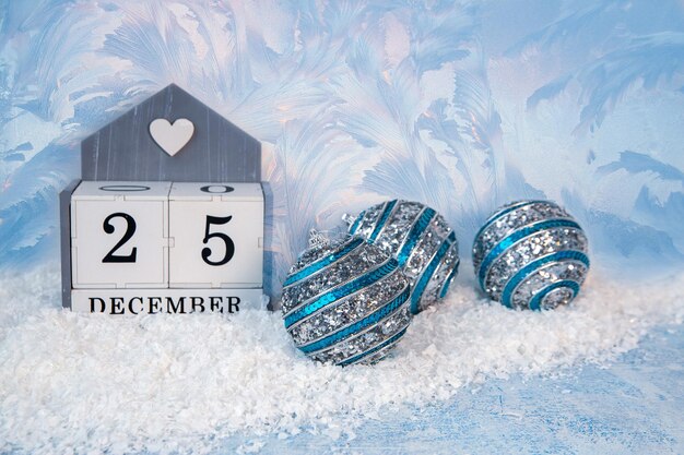 Christmas mood New Year background Sparkling Christmas balls on the snow and a calendar with the date December 25 with copy space The atmosphere of the holiday