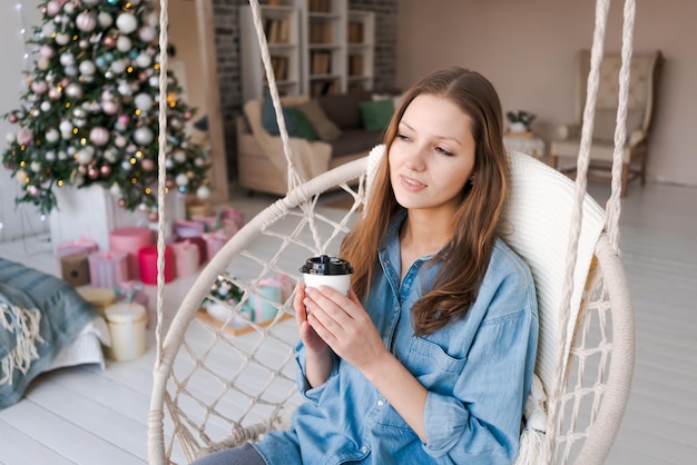 Christmas morning Christmas Girl on chair drinks from disposable paper cup