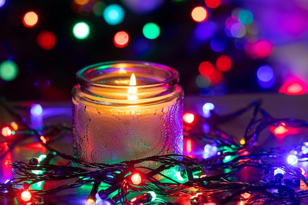 Christmas and New Year card with a candle and colorful garlands on a dark background