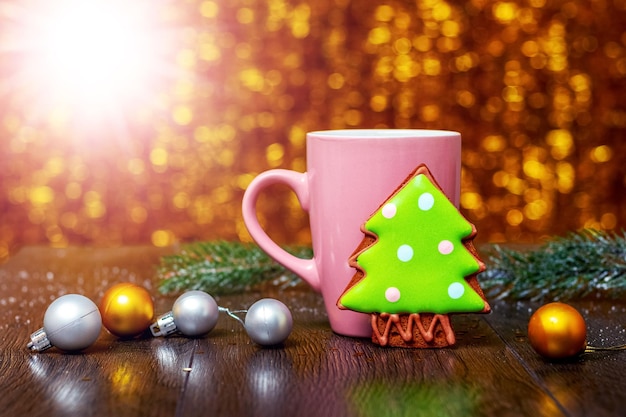 Christmas and New Year card with cookies next to cup of hot tea and fir tree branch with Christmas decorations and shiny bokeh background