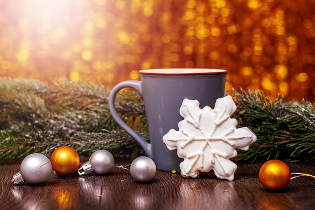 Christmas and New Year card with cookies next to cup of hot tea and fir tree branch with Christmas decorations and shiny bokeh background