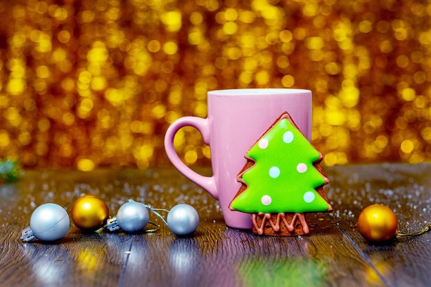 Christmas and New Year card with cookies next to cup of hot tea and fir tree branch with Christmas decorations and shiny bokeh background