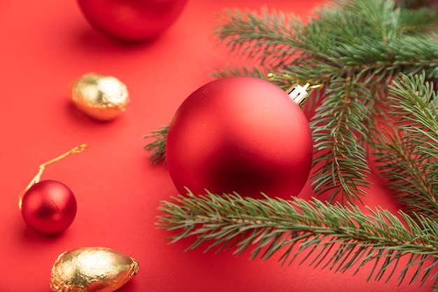 Christmas or New Year composition. Decorations, red balls, fir and spruce branches, on a red paper background. Side view, selective focus, close up.