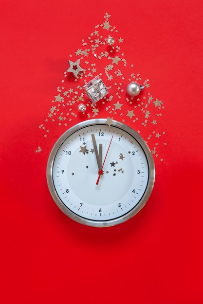 Christmas or New Year composition on red background with modern alarm clock and Christmas decorations - stars, confetti, balls and gift boxes, top view, flat lay