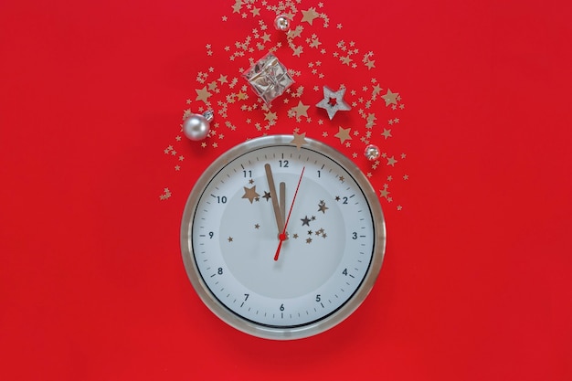 Christmas or New Year composition on red background with modern alarm clock and Christmas decorations - stars, confetti, balls and gift boxes, top view, flat lay