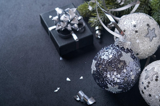 Christmas or New Year concept with black and silver baubles ball, gift box and champagne with decorated silver metallic ribbon on black background. Happy New Year 2022. Mock up.