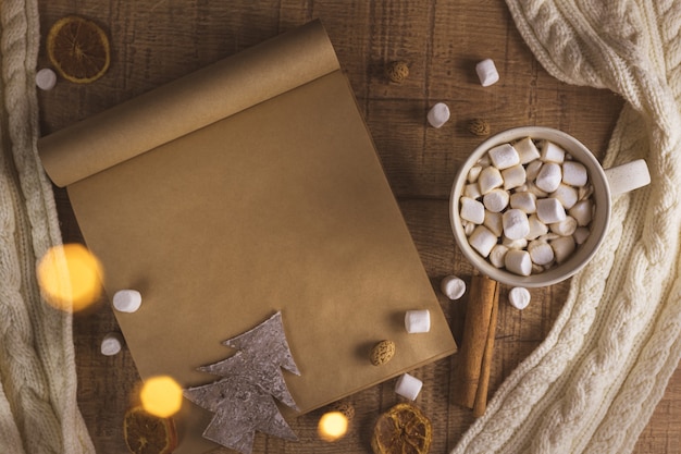 Christmas new year concept with cup of coffee with marshmallows and notepad. with copy space. scarf, lights