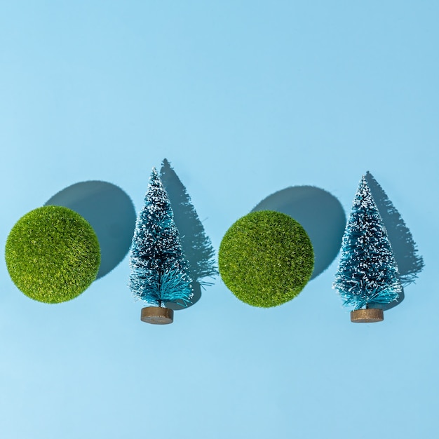 Photo christmas and new year conceptual background with small christmas trees and green balls on blue background. trendy hard shadows, studio shot.