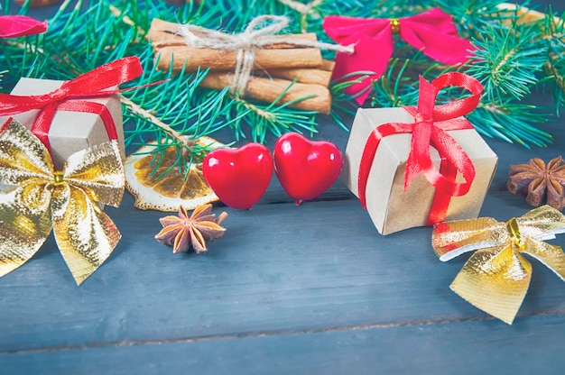 Christmas New Year decoration, fir branches, gift boxes with red bows, two red hearts on a wooden background close-up.