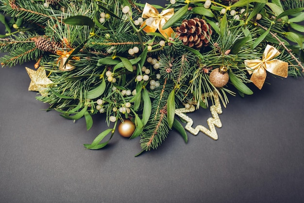 Christmas and New Year decoration made of fir, pine, mistletoe branches, cones with golden ornaments, toys. bows on grey background. Space