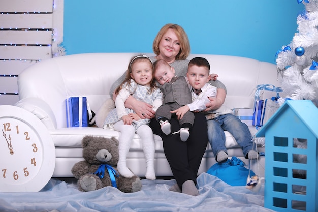 Christmas and new year holiday. grandmother with her little grandsons and granddaughter on a white sofa near christmas tree and gifts.