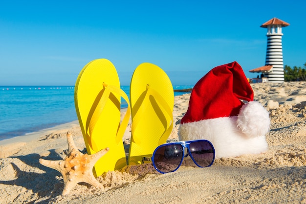 Christmas and New Year holidays at the sea. Santa hat, sandals, sunglasses on sandy beach