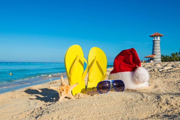 Christmas and New Year holidays at the sea. Santa hat, sandals, sunglasses on sandy beach