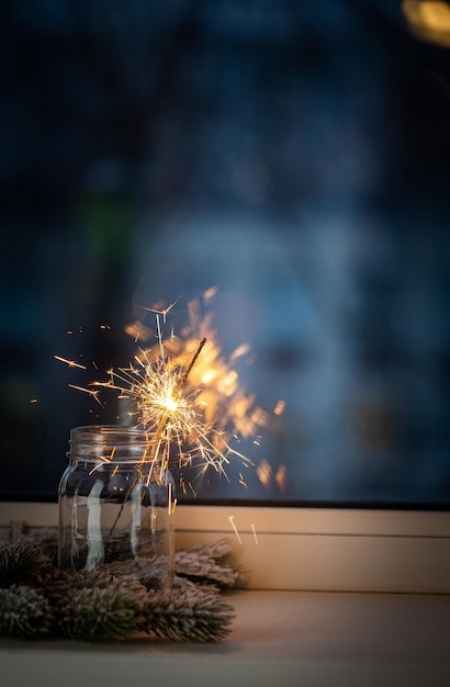 Christmas or new year party sparkler in a jar in front of the window on dark background xmas decoration