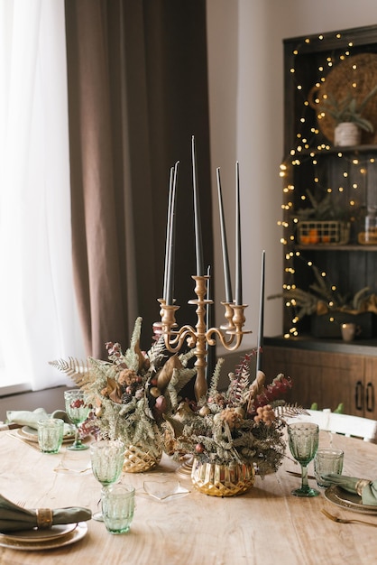 Photo christmas and new year's decor of the dining table candles in a classic candlestick glasses compositions of fir branches in golden vases