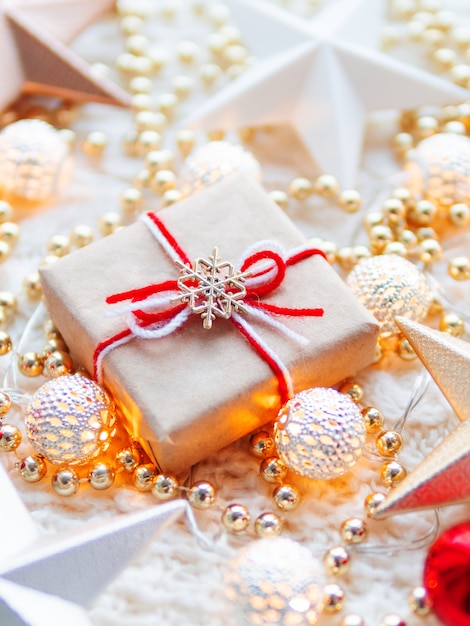 Christmas and New Year star decorations on white knitted . Present box wrapped in craft paper with snowflake symbol on it, metal light bulbs with delicate pattern, golden beads, red balls.