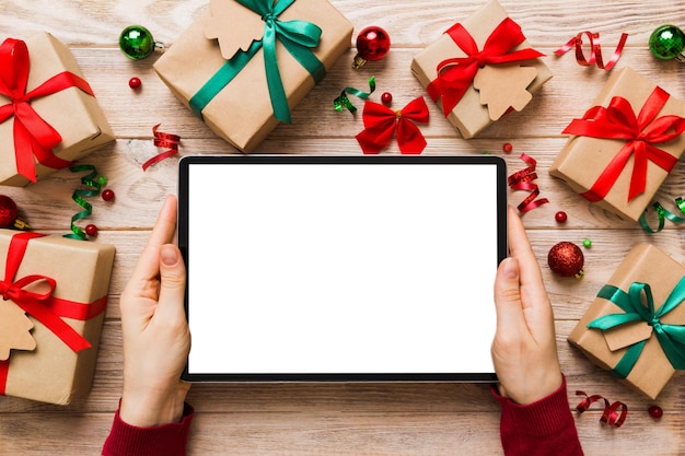 Christmas online shopping from home female hands holding tablet pc with blank white display top view woman hand holding tablet with blank screen Christmas tree and gifts on background