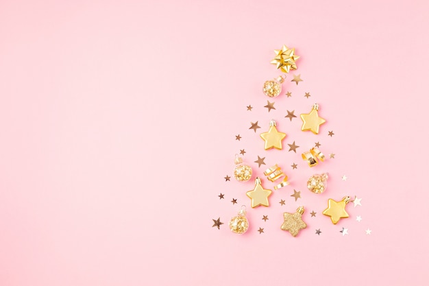 Christmas ornamets laid out in shape of Christmas tree on pink surface