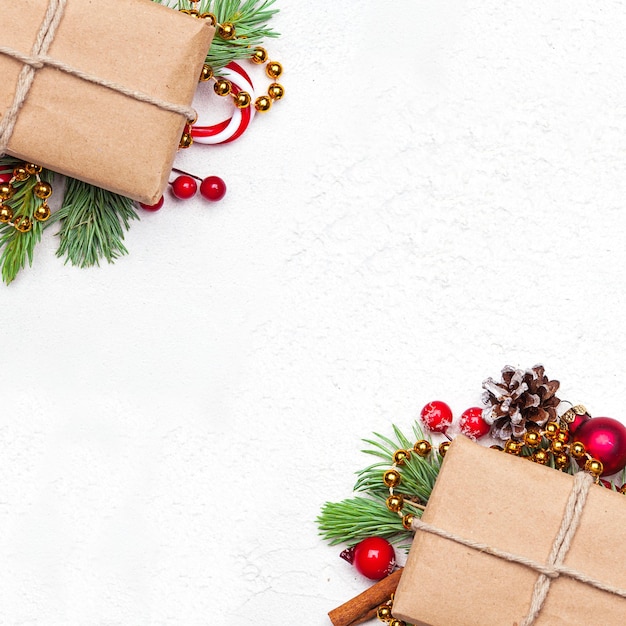 Christmas paper gifts with green Xmas fir branch red holly berries and baubles on white stucco plaster texture background Christmas composition top view flat lay with copy space