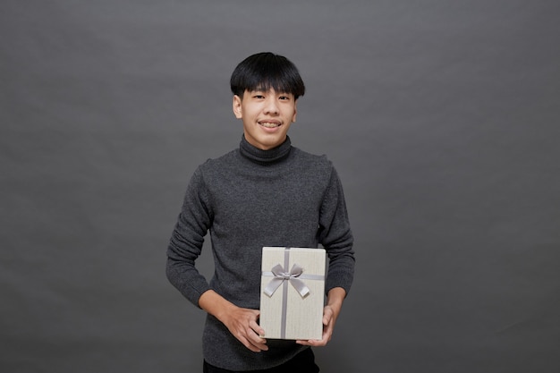 Christmas party and holidays concept. young Asian man holding gift box studio shot, Isolated on gray background