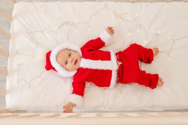 Christmas photo of a baby in a Santa suit lying in a crib at home