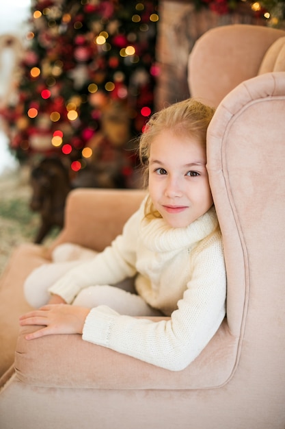 Christmas portrait of happy blonde child girl in white sweater siting on the floor