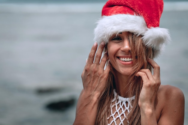 Photo christmas portrait smiling young woman in red santa hat close-up.christmas beach vacation travel woman wearing santa hat enjoying christmas on tropical beach.