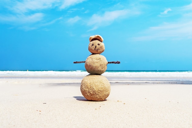 Christmas positive Sandy Snowman in red Santa Claus hat at ocean sunset beach. New Year vacation discounts in hot countries destinations concept