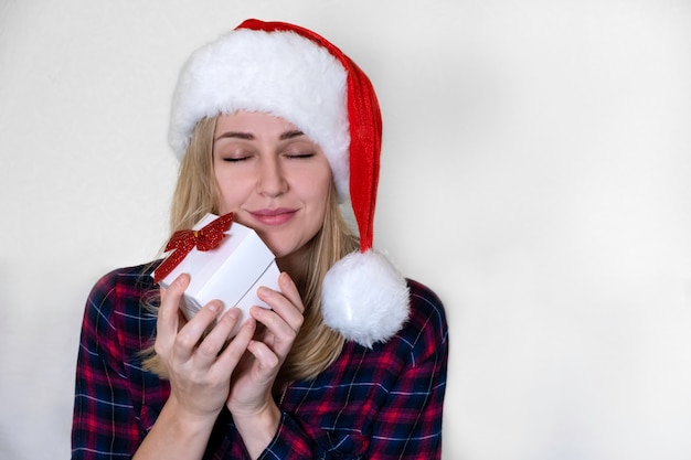 Christmas present. Young Caucasian woman with gift in her hands smiles and enjoys closing her eyes against a white background