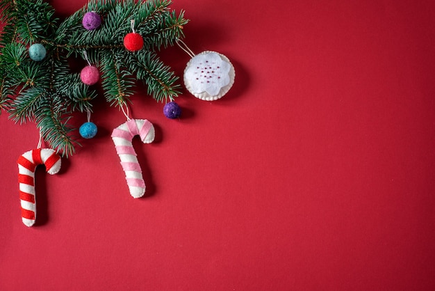 Christmas red bakckground with Christmas tree branch decorated with handmade Christmas ornaments: felt candy canes and Christmas baulbs with copy space