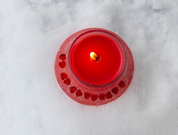 Christmas red burning candle in the transparent glass candlestick on snow background