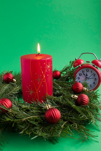 Christmas ring or wreath red burning candle and alarm clock on the green background Closeup Location vertical