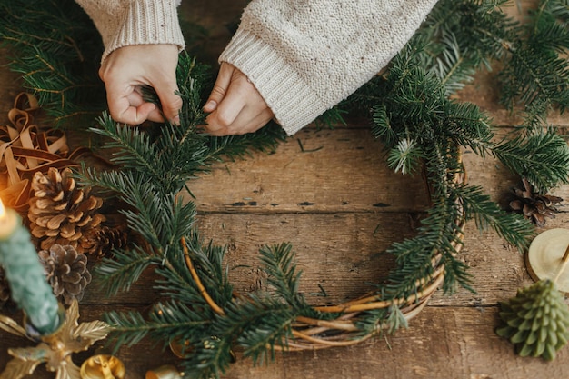 Christmas rustic wreath Female hands holding fir branches and making wreath on wooden table