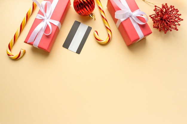 Christmas shopping concept. Gift boxes, lollipops cane and credit card on beige background, space for text