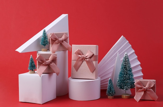 Christmas showcase Geometric shapes mini Christmas trees and gift boxes on red background Concept art minimalism