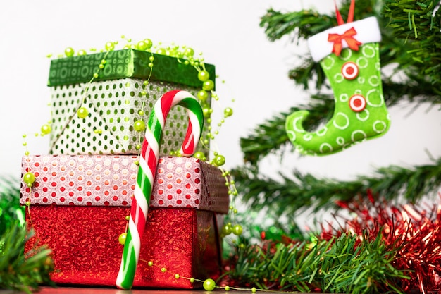 Christmas spirit. A pair of gifts packed in a bright festive packaging, next to which is a bright lollipop in the form of a cane, located on a wooden table next to the Christmas tree.