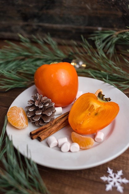 Christmas still life with fresh persimmon with pine cones, cinnamon, marshmallow and mandarine