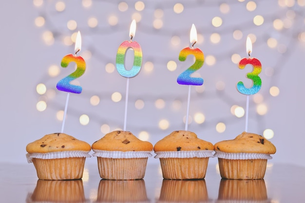 Christmas sweet cupcakes and burning candles in form of numbers 2023. White background with bokeh.