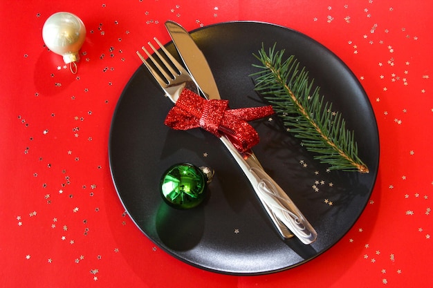 Christmas table setting in black plate with color balls on red table copy space Christmas dinner