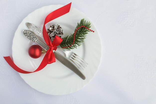 Christmas table setting on the white plate on the white textile background. Top view. Copy space.