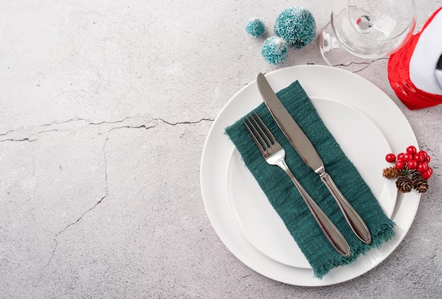 Christmas table setting with white dishware silverware and red and green decorations on white wooden background Top view