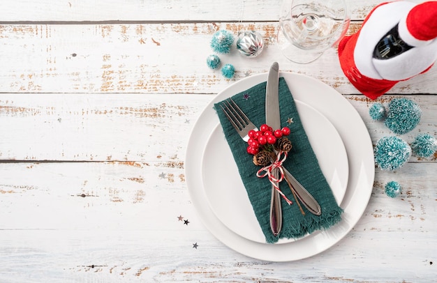 Christmas table setting with white dishware silverware and red and green decorations on white wooden background Top view