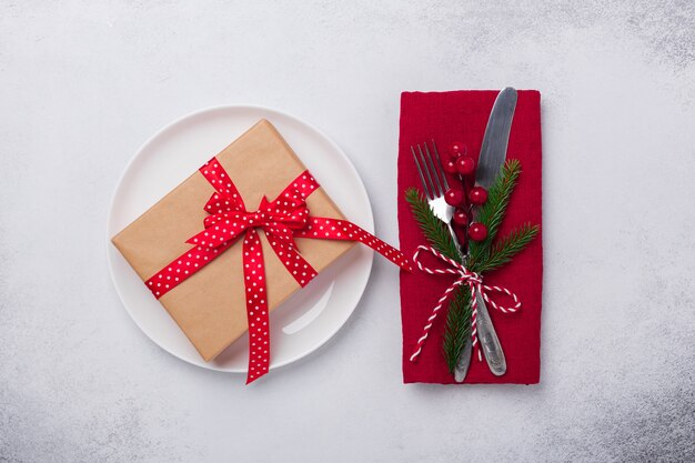 Christmas table setting with white plate, gift box and silverware on stone background